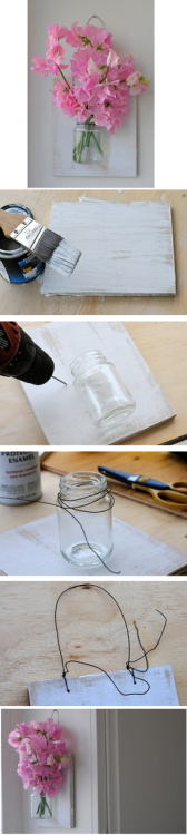 Making a vase for on the wall… 

step one
Buy  or find a piece of wood to use that is in proportion to the jar, which  you also need to find or buy. If you are like me you will have the  chance to recycle one. Make sure the jar (or use a vase) has a lip on  the top. Paint the wood however you would like it.
step two
Position the jar on the wood and drill two holes on either side at the the base of the opening. 
step three
Wrap  steel wire around the lip of the jar a few times and twist it once   until it’s secure.  Position the jar so that it’s lined up on the wood   and poke the ends through the small holes that you drilled.  Wrap them   together in the back and clip any extra wire.
step four
Drill  two additional holes at the top of the wood and wrap a second  piece of  steel wire through leaving a large loop at the top.  Twist the  ends  around the base and clip off the extra wire.
Add water and flowers then hang it up.  Dried or imitation flowers could also be used.
It really was that simple! Fun to make :)