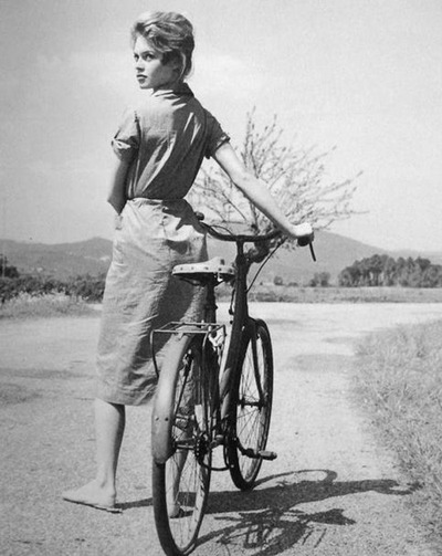 Brigitte Bardot walks a bike. 